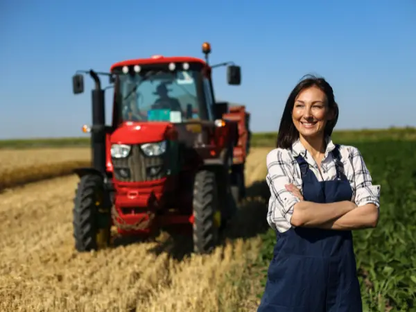 Una mujer posa en su explotación, con un tractor de fondo.