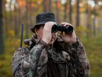 Cazador con ropa de camuflaje observa el terreno a través de unos prismáticos.