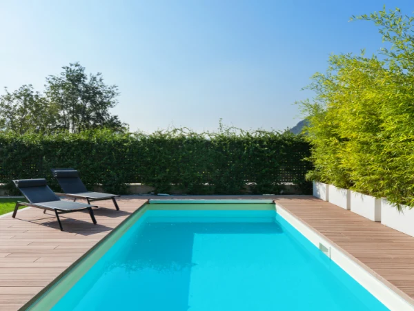 Piscina en terreno rústico con tarima de madera, rodeada de vegetación y tumbonas.