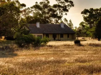 Casa de campo entre árboles y pasto seco al atardecer en una finca rústica.